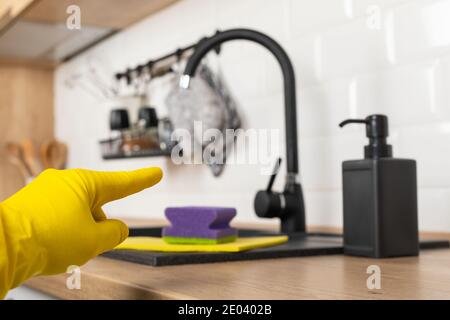 Housekeepers hand holding cleaning supplies in front of black kitchen sink Stock Photo