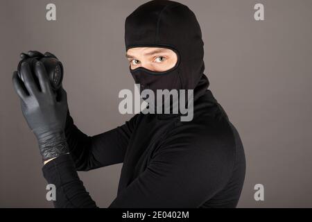 Picture of a thief dressed in black costume and wearing mask trying to turn off surveillance camera Stock Photo