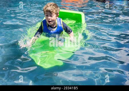 Young boy in swimming pool with green plastic boat having summer fun. Stock Photo