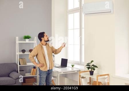 Man standing in living-room and switching on air conditioner with remote control Stock Photo