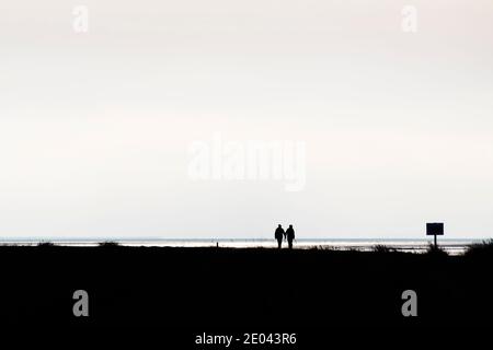 Silhouette of couple holding hands at the beach in winter. Stock Photo