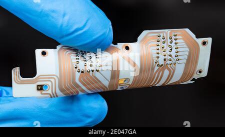 Flex printed circuit board in man fingers isolated on a black background. White PCB sheet with integrated connector for computer printer printhead. Stock Photo