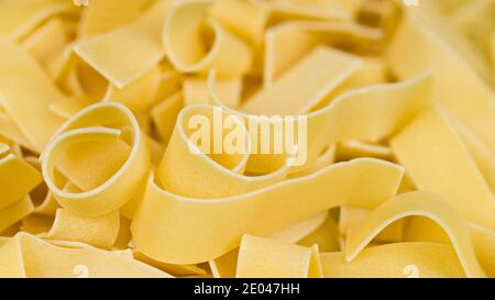 Close-up of wide flat noodles pile in beautiful pasta background. Yellow raw dried ribbon tagliatelles in abstract culinary texture. Selective focus. Stock Photo