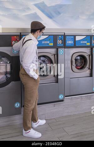 selective focus of a teenager with straps setting off the washing machine with the dirty clothes to be washed automatically Stock Photo