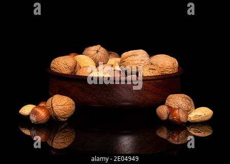 Wooden Bowl with walnuts, almonds, pecans, hazelnuts in shell on black reflective surface Stock Photo