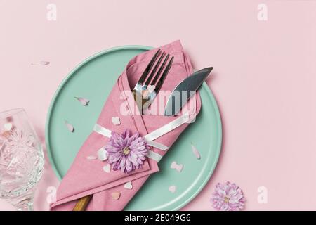 Beautiful festive table setting with green plate, napkin, flowers and hearts decoration on pastel pink background. Top view with copy space. Stock Photo