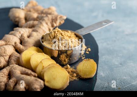 Fresh ginger root and ground ginger spice in black bowl on blue background. Stock Photo