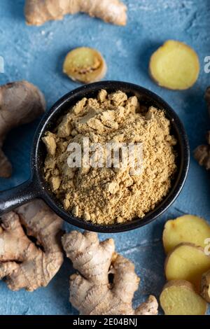Fresh ginger root and ground ginger spice in black bowl on blue background. Stock Photo