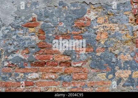 old red and yellow bricks on the wall texture with pieces of plaster and paint Stock Photo