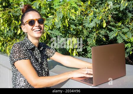 Young woman remotely working at outside location. Medium shot. Laughing at camera Stock Photo