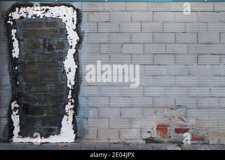 Photograph of a weathered brick wall with a black bricked-up door framed by white paint Stock Photo