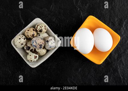 Three quail eggs and chicken eggs on black background Stock Photo