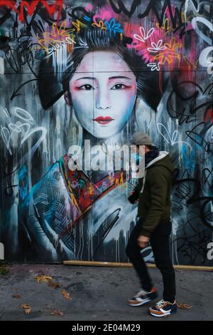 London, UK. 24 Dec 2020. A man in a face mask walks past a mural of a beautiful Geisha in Spitalfields. Street Art London. Credit: Waldemar Sikora Stock Photo