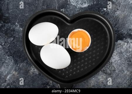Two white eggs and yolk on heart shaped pan Stock Photo