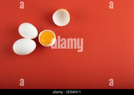 Broken and whole raw eggs on red background Stock Photo