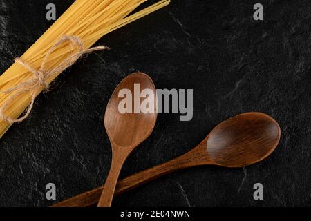 Raw spaghetti and wooden spoons on black background Stock Photo
