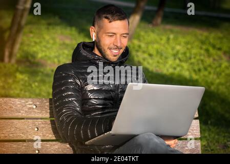 Happy young smiling man working with laptop outdoor in the city park. Student studying outside. Freelance working concept Stock Photo