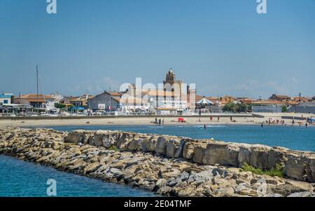 harbour seawall of Port Saintes-Maries-de-la-Mer with view of Arena Beach and the fortified church in the background, Bouches-du-Rhône department, Sou Stock Photo