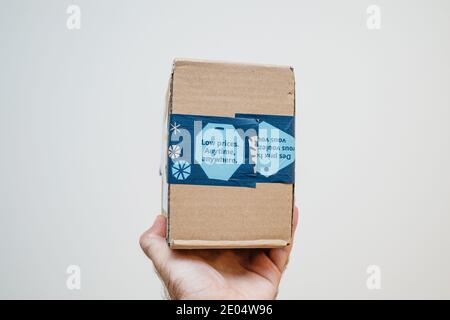 Paris, France - Dec 12, 2020: POV male hand holding parcel package from Amazon Prime with Low Price Anytime, Anywhere advertising on the package - isolated on white Stock Photo