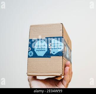 Paris, France - Dec 12, 2020: POV male hand holding parcel package from Amazon Prime with Low Price Anytime, Anywhere advertising on the package - isolated on white Stock Photo
