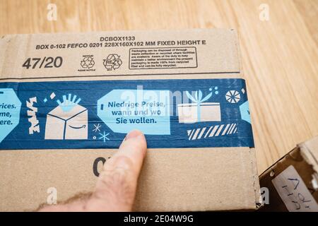 Paris, France - Dec 12, 2020: POV male hand pointing to german words transalted as Low Price Anytime, Anywhere advertising on the package of Amazon Prime winter Christmas holiday scotch band Stock Photo