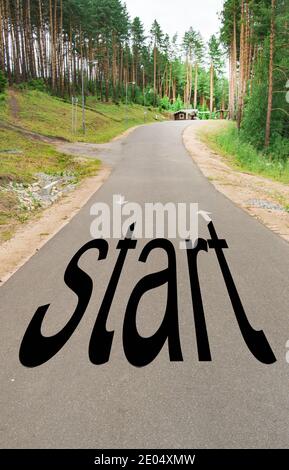 The word START is written on the highway in the middle of an empty asphalt road in a natural Park, between tall pines Stock Photo