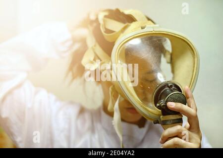 A Asian woman pulling on a full face protective oxygen mask, white coat and rubber gloves, getting ready to work at a biochemical lab. Stock Photo