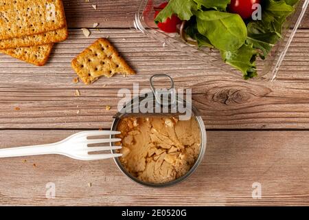 Flat lay image of quick and snack photo featuring a easy open can of tuna with tuna chunks in oil on wooden table or bench, clear plastic container wi Stock Photo