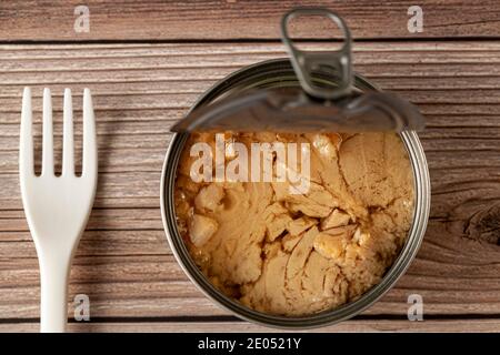 A simple, quick and convenient snack photo featuring a easy open can of tuna with tuna chunks in oil on wooden table or bench with a disposable plasti Stock Photo