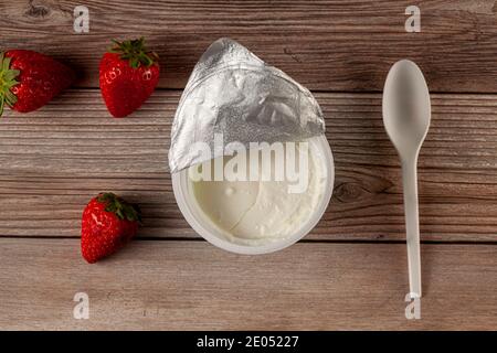 Flat lay image of a store bought plastic cup of plain low fat Greek Yogurt with the aluminum foil seal peeled off. It is on wooden background with a p Stock Photo