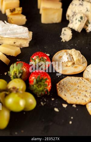 A vertical image of a cheese platter containing a selection of aged artisan French, Italian and Swiss cheese assortment on black cheese board served w Stock Photo