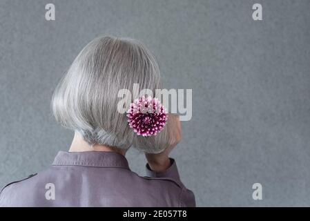 Silver-haired lady with red dahlia flower, on gray background with copy space.