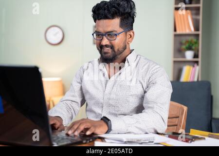 Happy young man busy working on laptop at home - concept of professional IT employee during work from home. Stock Photo