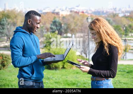 African black man and redhead caucasian woman working with laptop and tablet in a park. Young multiracial couple. Stock Photo