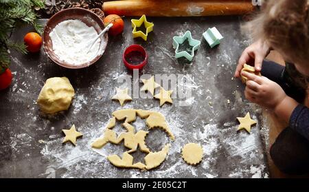 A cute little girl 3-4 years old sits on the windowsill and prepares Christmas cookies. Family vacation at home during the holidays. New Year's and Ch Stock Photo