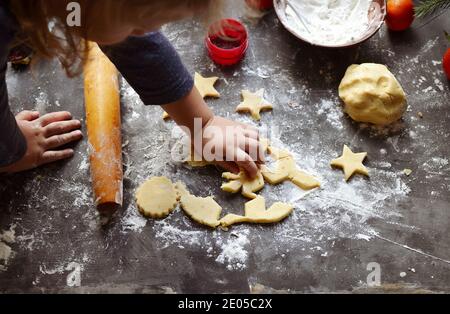 A cute little girl 3-4 years old sits on the windowsill and prepares Christmas cookies. Family vacation at home during the holidays. New Year's and Ch Stock Photo