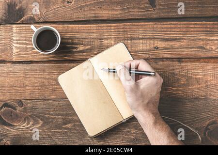 Simple work place. Wooden office desk table,  with hand writing on an empty notebook, and coffe. Morning planner concept. Stock Photo
