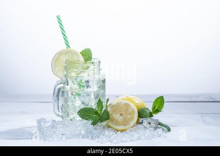 Pitcher of very refreshing lemonade with lemons, mint and ice, on white wood with hand squeezing lemon Stock Photo