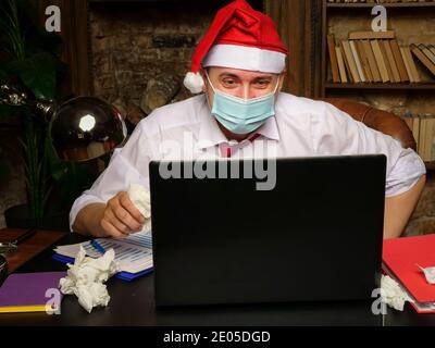 A sick man in a Santa hat communicates on the Internet. New year and quarantine. Stock Photo
