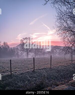 A frozen misty field at sunrise. The layers mist settle over the lower ground across a classic British countryside view at sunrise in winter. Stock Photo
