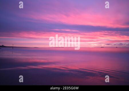 The sun paints the clouds with magical pink and purple colours as it rises into a winter sky on a cold morning on Bournemouth beach. Stock Photo