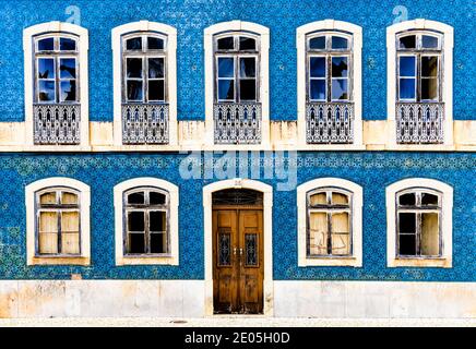 A frontal view of a house facade covered in azulejo tiles with broken windows and wooden door Stock Photo