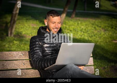 Young man working with laptop and headphones in the city park. Student studying outside. Freelance working concept Stock Photo