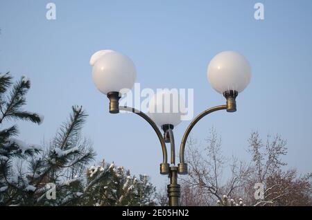 Iron lantern with three round plafonds, covered with snow and icicles in winter, on the background of the sky and Christmas trees Stock Photo