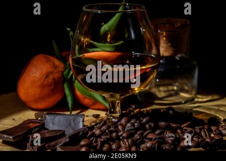 Glass of brandy on wooden table with close chocolate, coffee and mandarins. Stock Photo