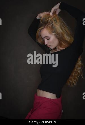 A fit healthy naturally beautiful young woman (20)  with strong features stretches upward showing slim athletic waste in a confident pose. Stock Photo