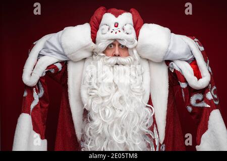 father frost in long warm coat, red mittens and a hat panics and holds his head Stock Photo