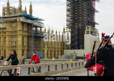 Scottish man traditionally dressed in a kilt plays traditional music from Scotland on bagpipes outside Houses of Parliament on Westminster Bridge. Stock Photo