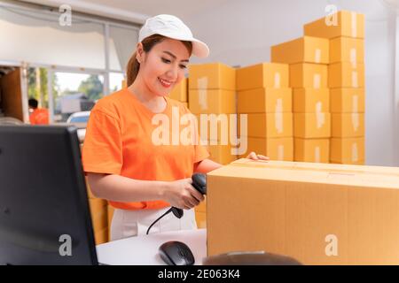 Asian parcel delivery worker in warehouse with barcode scanner. Stock Photo