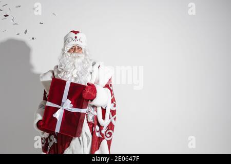 Santa Claus with red xmas gift posing in studio, elderly male with christmas present, copy space for holiday advertising Stock Photo
